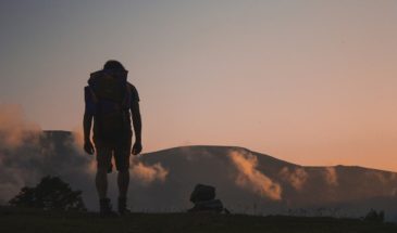 Un randonneur en excursion se trouve debout face aux montagnes admirant le paysage.