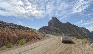 Trekking Oman : une voiture blanche sur une route Oman avec une vue sur un paysage désertique orangé apaisant lors de cette traversée.