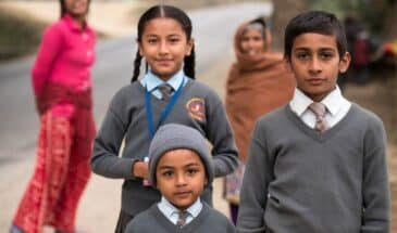 Écoliers Népal : il y a des enfants en uniforme et on peut apercevoir derrière deux femmes qui les regardent.