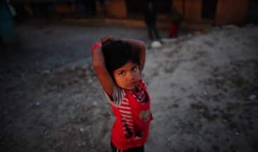 Enfant Népal : on voit un enfant debout avec les mains sur la tête. Il est sur des sentiers.