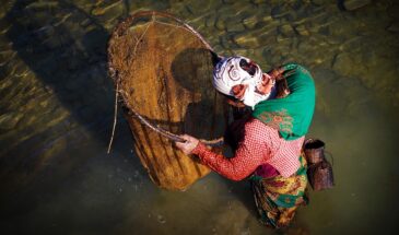Femme pèche rivière Népal : il y a une femme habillée dans la rivière, elle tient une sorte de filet de pêche.