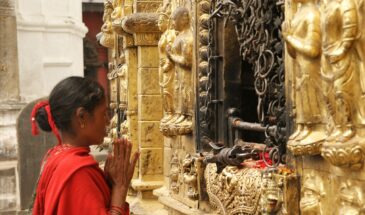 Femme prière Népal : on voit une femme face à des statues, qui ferment les yeux et joint les deux mains.