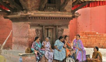 Femmes assises Népal : il y a des femmes qui discutent assises sur des pierres, sous un édifice.