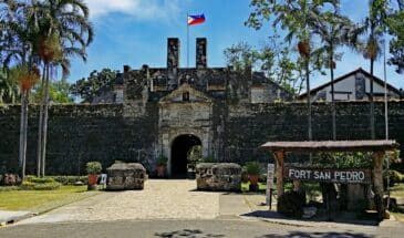 Fort San Pedro Cebu : il y a une bâtisse ancienne en pierre, avec des palmiers et une petite cabane à l'avant.