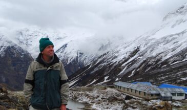 Homme randonneur Népal vue : on voit un homme qui regarde vers les montagnes. Plus bas, il y a une maison.