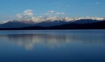 Lac Rara : il y a des végétations au bord du lac, au loin il y a des montagnes enneigé.
