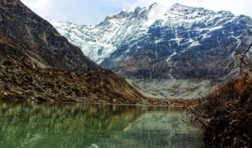 Monument montagne Népal : il y a un lac avec au bord des écorces. Le sommet des montagnes est enneigé.