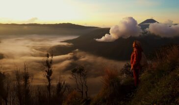Randonnée Bali : une jeune randonneuse, portant un sac à dos, habillée en rouge sur une montagne nuageuse.