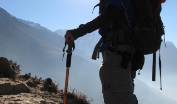 Randonneur sentier Népal : il y a un homme en excursion dans les montagnes. On aperçoit le soleil et des rochers.