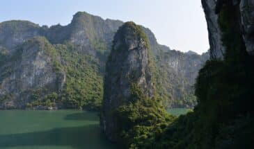 Rochers baie d'Halong Vietnam : il y a une rivière et des grandes roches avec de la verdure dessus.