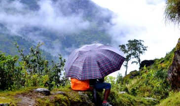 Trekking Népal : il y a une personne assise sur la végétation, avec un parapluie sur la tête.