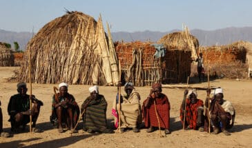 Une Tribu en Éthiopie assis sur le sable dans le désert avec des cases faites en paille à l'arrière