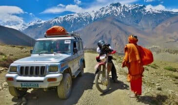 Voyage 4x4 Népal : il y a une voiture et une moto. Le motard prend la photo d'un népalais. Il y a des montagnes.