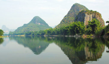 Minorités du Guizhou Circuit : un homme au milieu du lac en train de ramer et à l'horizon des montagnes.
