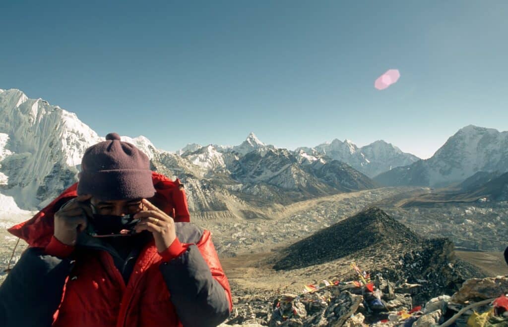 Culture népalaise : il y a un homme en randonnée dans les montagnes, derrière lui se trouve beaucoup des objets.