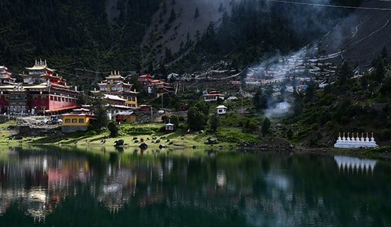 Découverte Région Kham-Amdo : un village chinois, posé au bas de la montagne avec un lac vert.