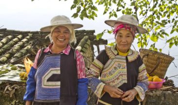 Ethnies Dong : 2 femmes du village chinois, portant des chapeaux, elles ont des fruits et une maisonnette.