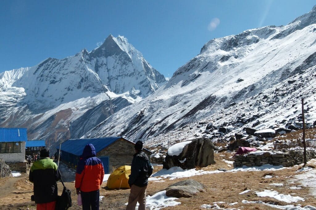 Machhapuchre trekking : il y a des randonneurs, devant des chalets avec des tentes. Ils sont au bord des montagnes.