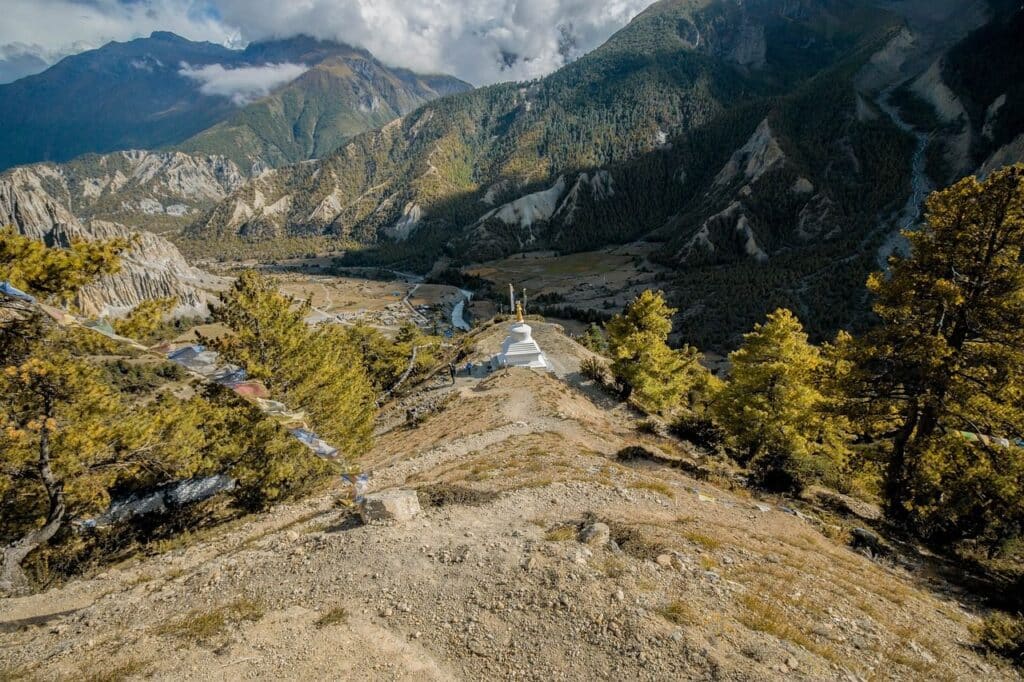 Népal trekking Annapurna : il y a un monument blanc au milieu des montagnes, il y a aussi de la végétation.