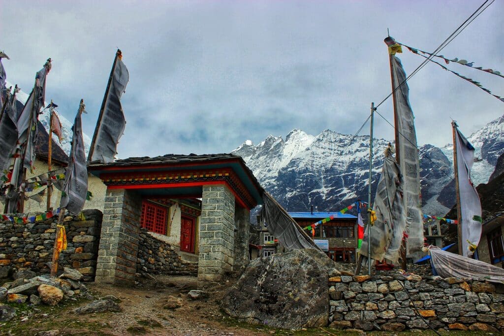 Randonnée Népal : il y a des bâtisses sont en pierre, il y a des voiles, et au loin des montagnes.