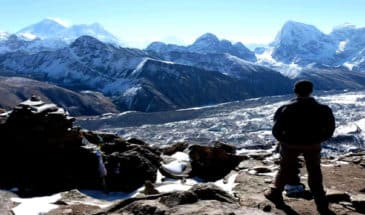 Trek au Népal : on voit un homme debout sur des pierres qui regarde les montagnes enneigées.