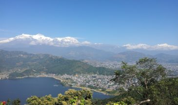Ville côtière Népal : il y a une ville au bord de mer. Elle est encerclée de végétation et de montagnes au loin.