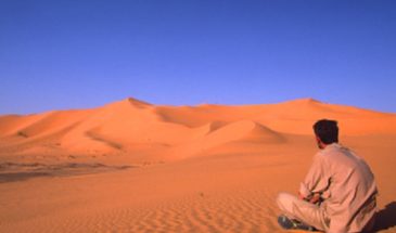 Un touriste assis sur le sable du désert observant le paysagede l'Erg Chech dans le Sud-Ouest