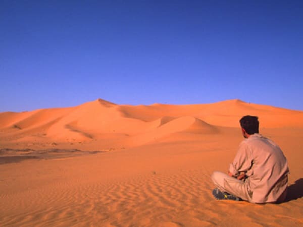 Un touriste assis sur le sable du désert observant le paysage de l'Erg Chech dans le Sud-Ouest