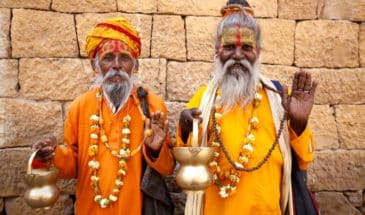 Brahmane Inde : des hommes seniors habillés en jaunes, tenant des coupes dorées, levant leurs mains gauches.