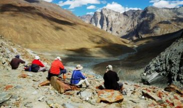 Des randonneurs assis dans la vallée en Inde, observant l'horizon montagneux, et un ciel nuageux bleu.