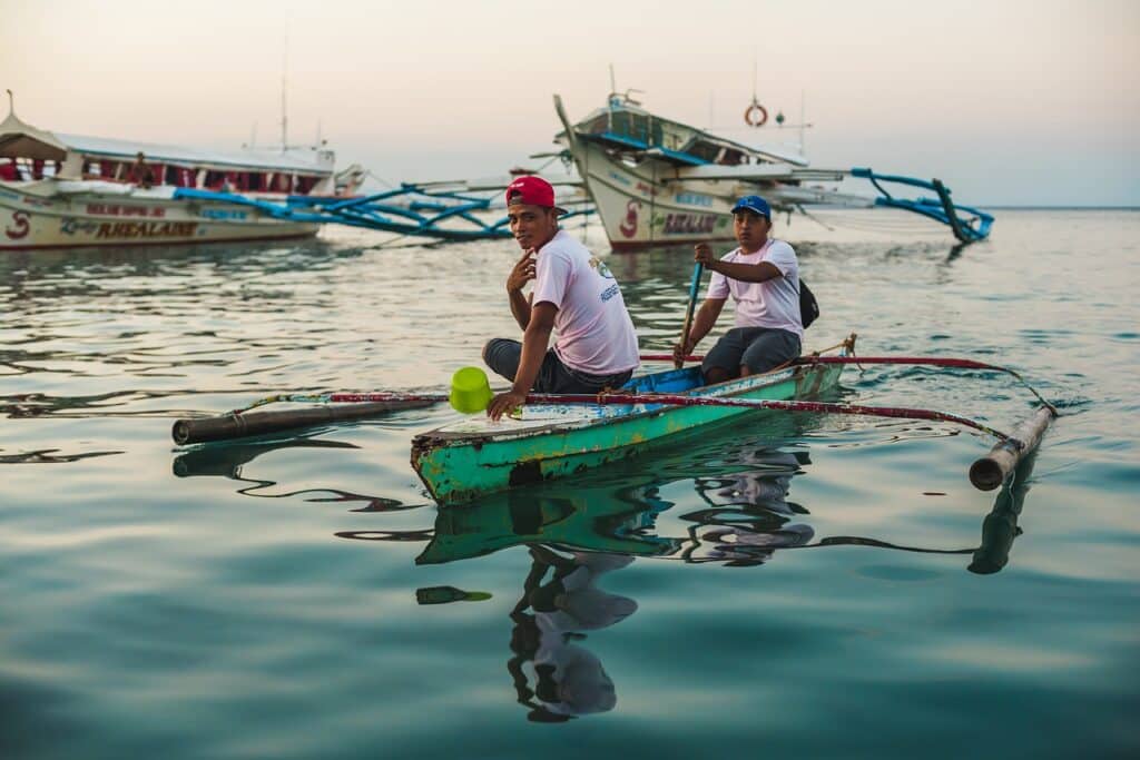 L'île de Mindoro, sur la mer il y a deux personnes sur une barque. En arrière-plan, il y a des grands bateaux.