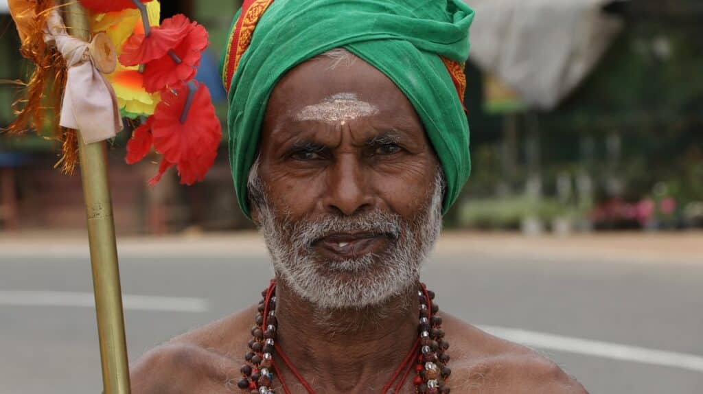 Séjour au Sri Lanka, un homme vêtu d'un accoutrement traditionnel, un foulard, des colliers et qui tient un bâton.