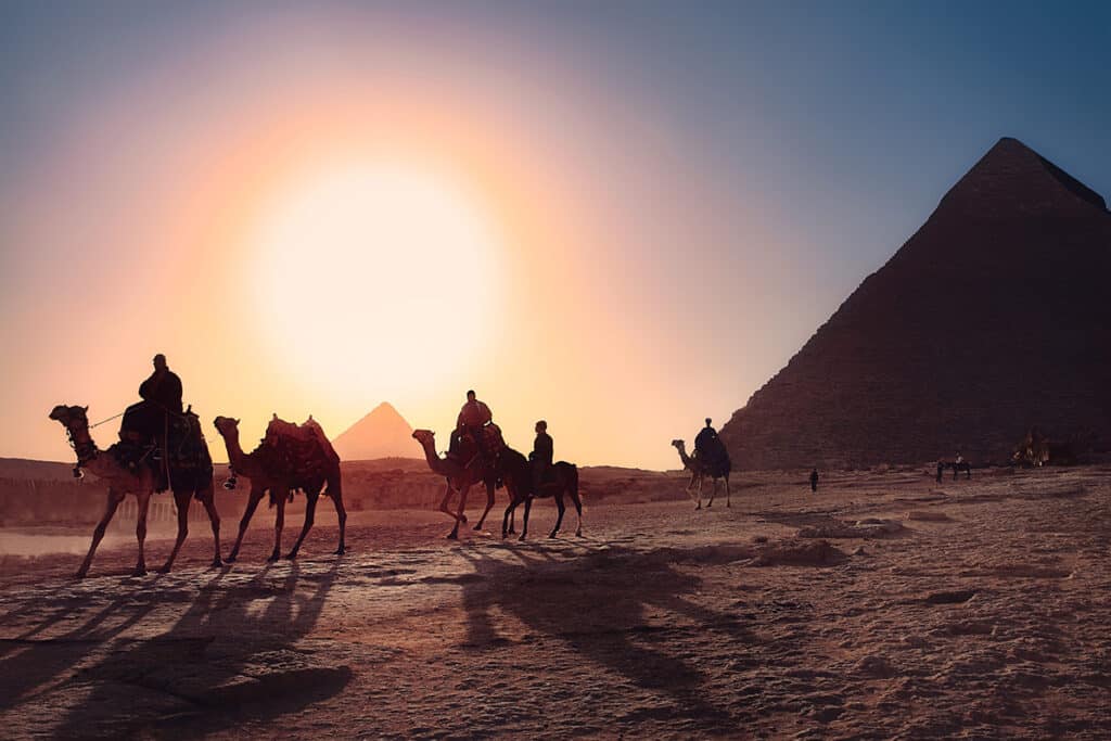 Trek dans le désert, randonnée chamelière guidée des touristes lors d'un coucher de soleil en Egypte