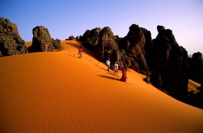 Trek Tam Djanet : touriste à pieds en découverte dans le désert rempli de sable et de massifs rocheux