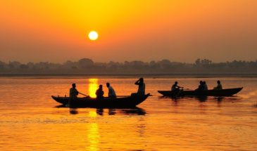 Voyage Gange : des hommes ramant sur des pirogues, sur un lac sous un coucher de soleil.