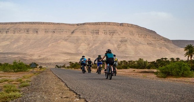 Escalade au Maroc : groupe de touristes en VTT sur une route aménagée dans une zone désertique.